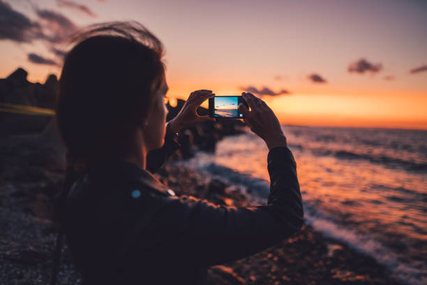 Человек фотографирует закат над океаном на iPhone.